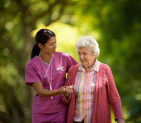 Feliz joven enfermera ayudando a un paciente anciano caminando afuera